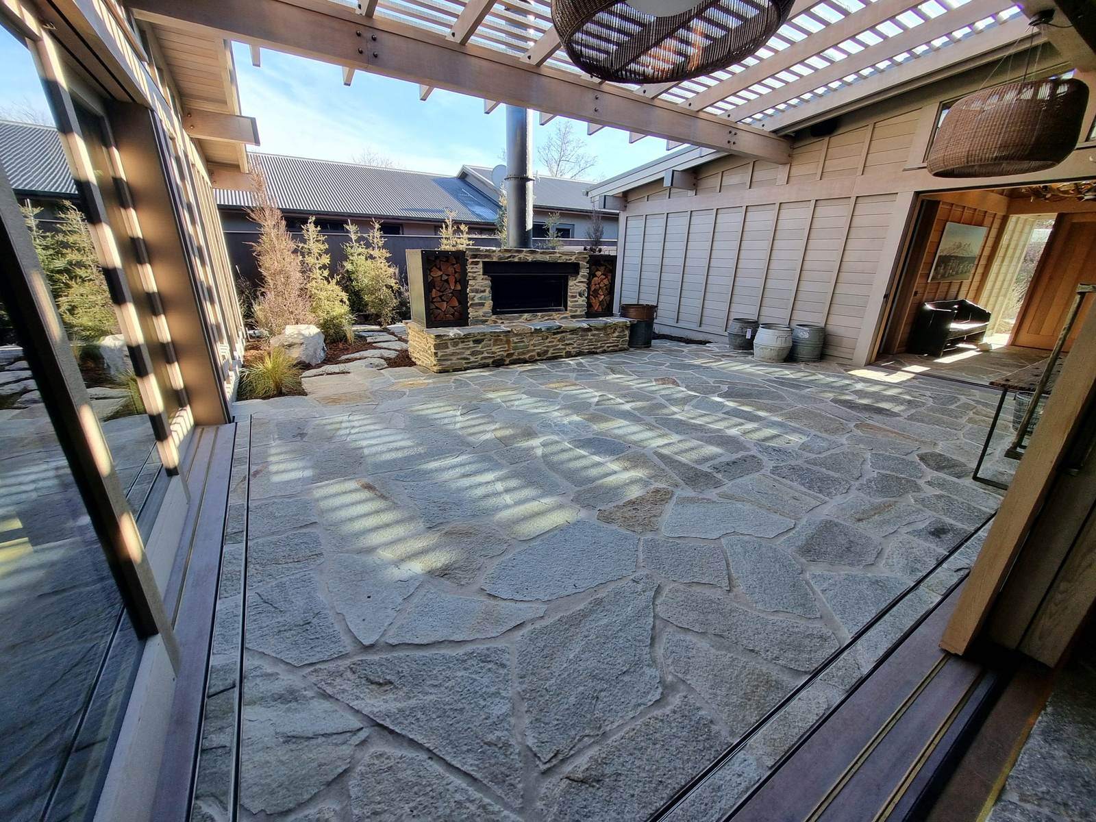 Natural stone crazy paving courtyard with outdoor fireplace under a pergola