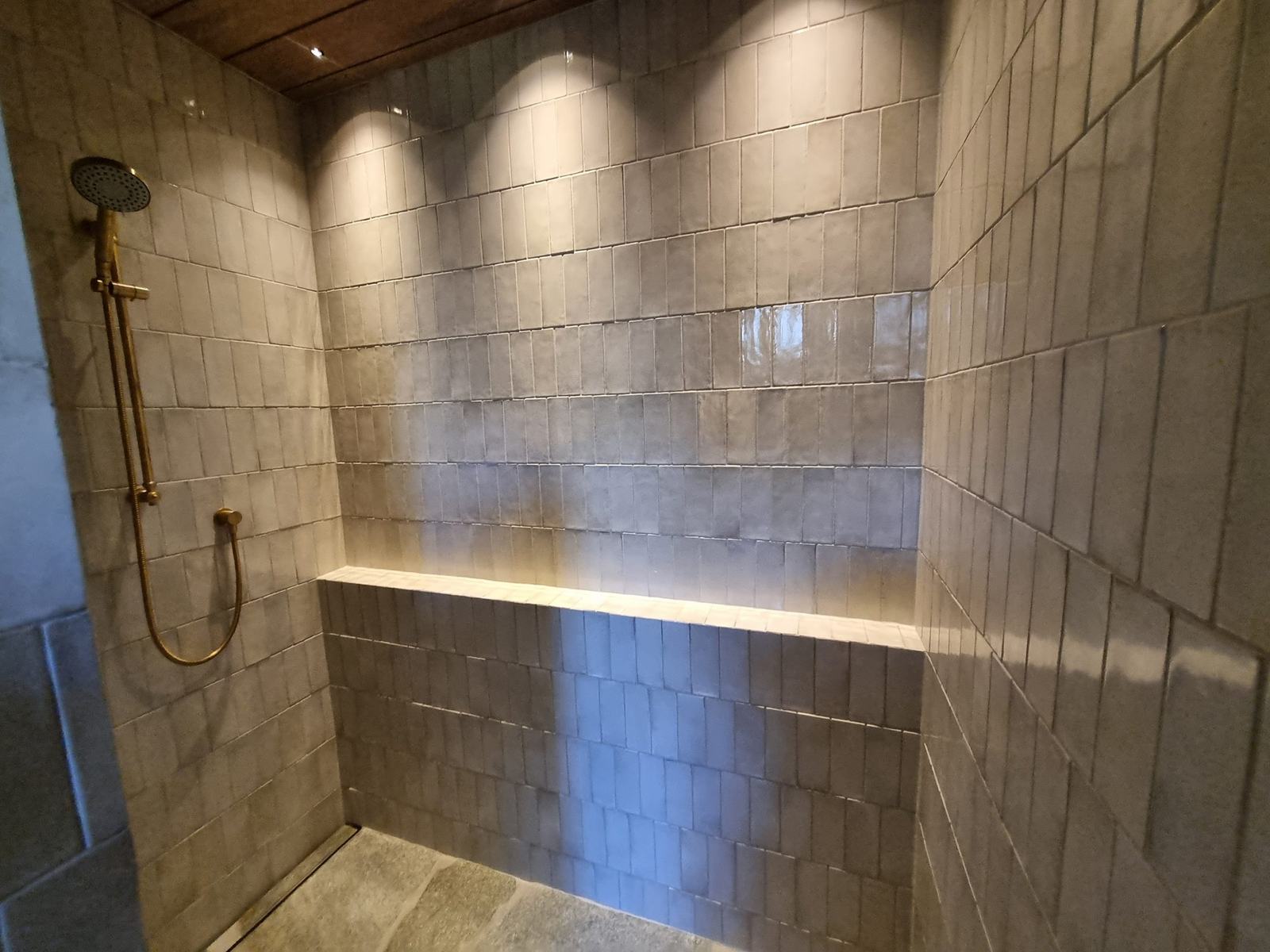 Zellige-style tiled shower with brass fittings and stone floor